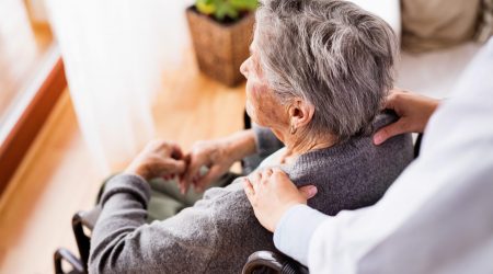 Health visitor and a senior woman during home visit. Unrecognizable nurse giving woman shoulder massage.